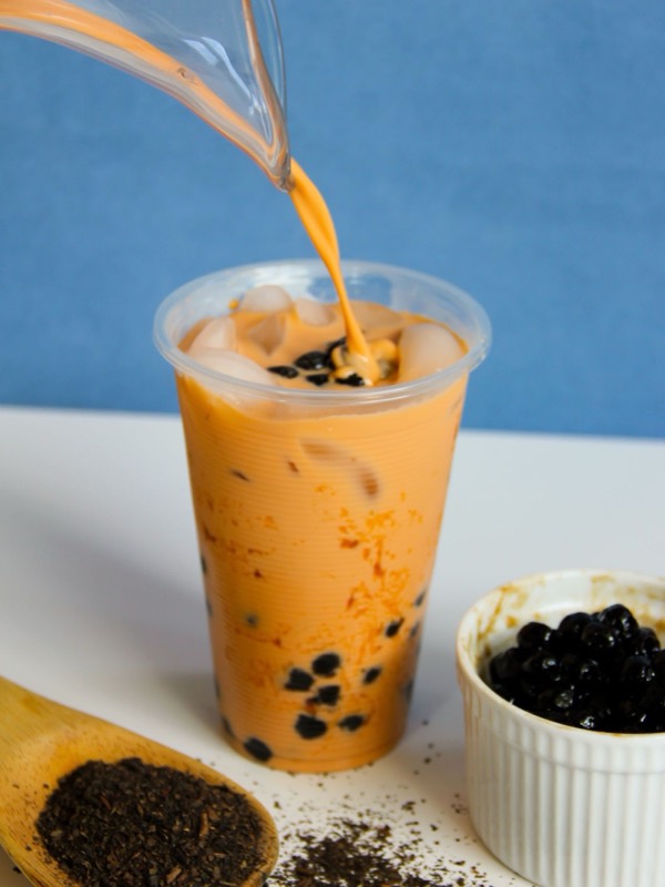 Milk tea being poured over tapioca pearls