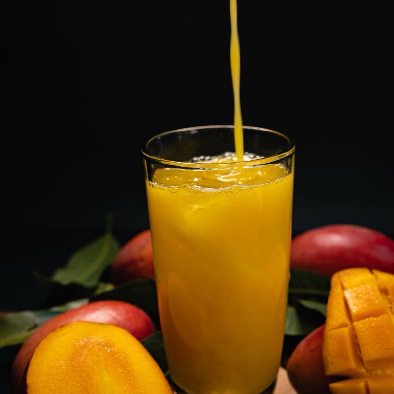 Mango juice being poured into a glass beside ripe mangoes